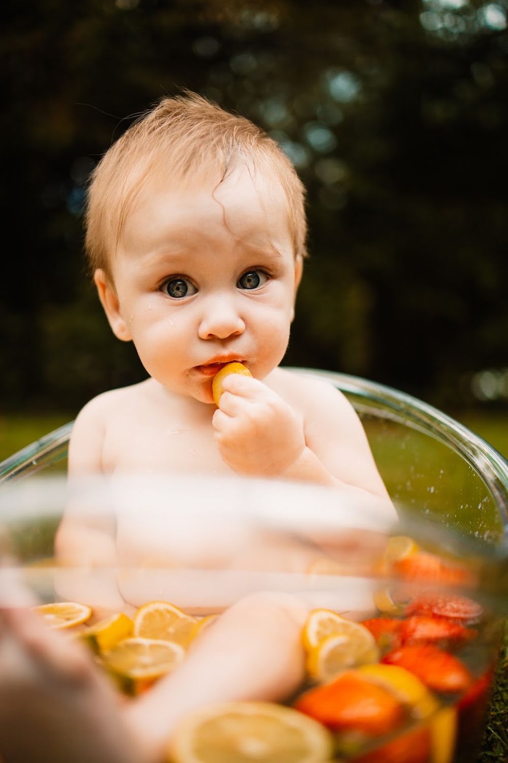 Cute baby sitting in a glass bowl with citrus fruit slices, eating an orange slice outdoors in Oak Ridge, TN.