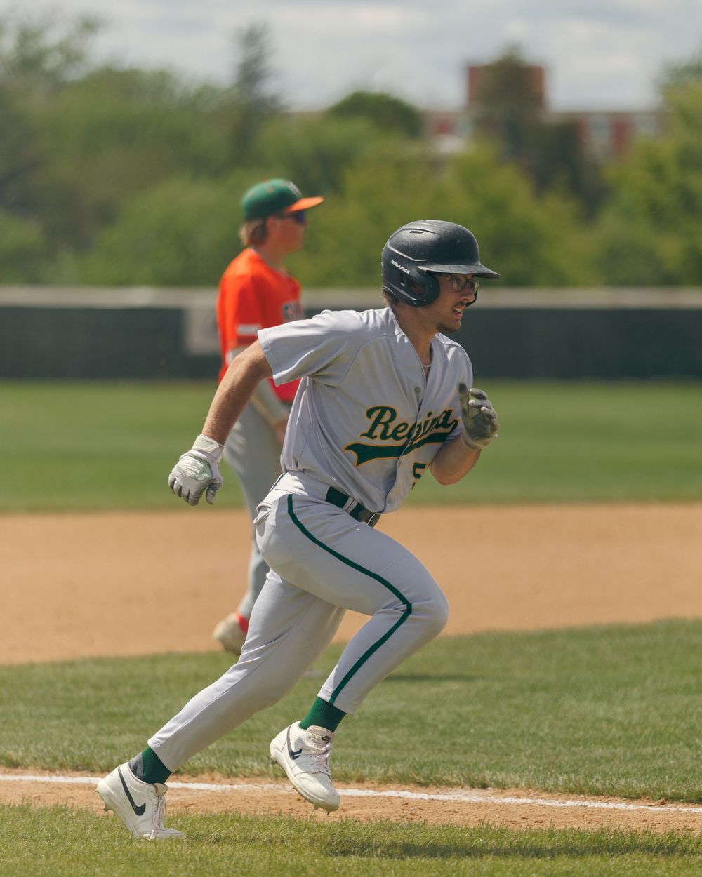 A Regina baseball player sprints down the baseline during a sunny game.