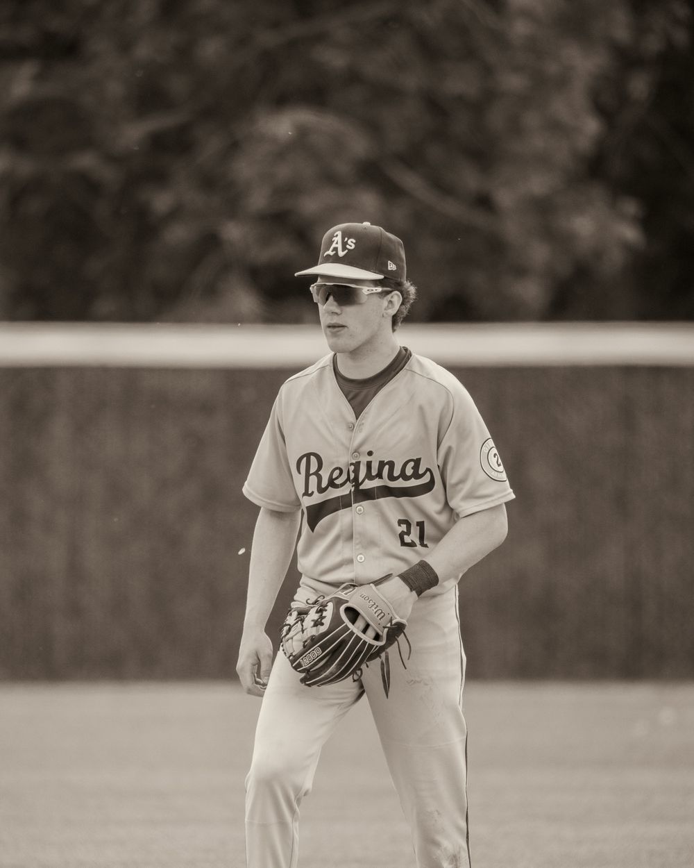 A Regina Athletics baseball player wearing sunglasses stands ready in the field.