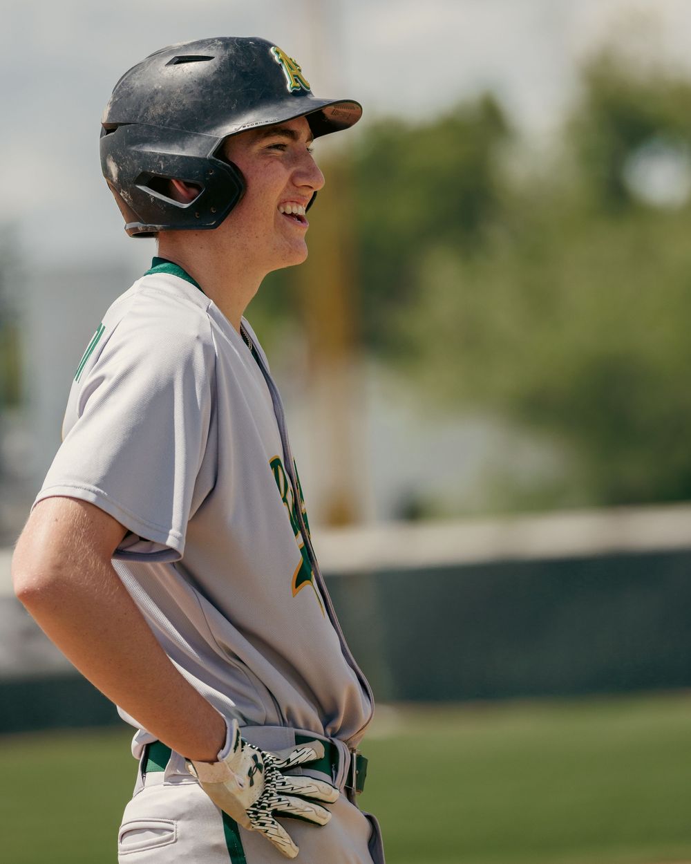 A smiling baseball player in a green and gray uniform stands on the field.
