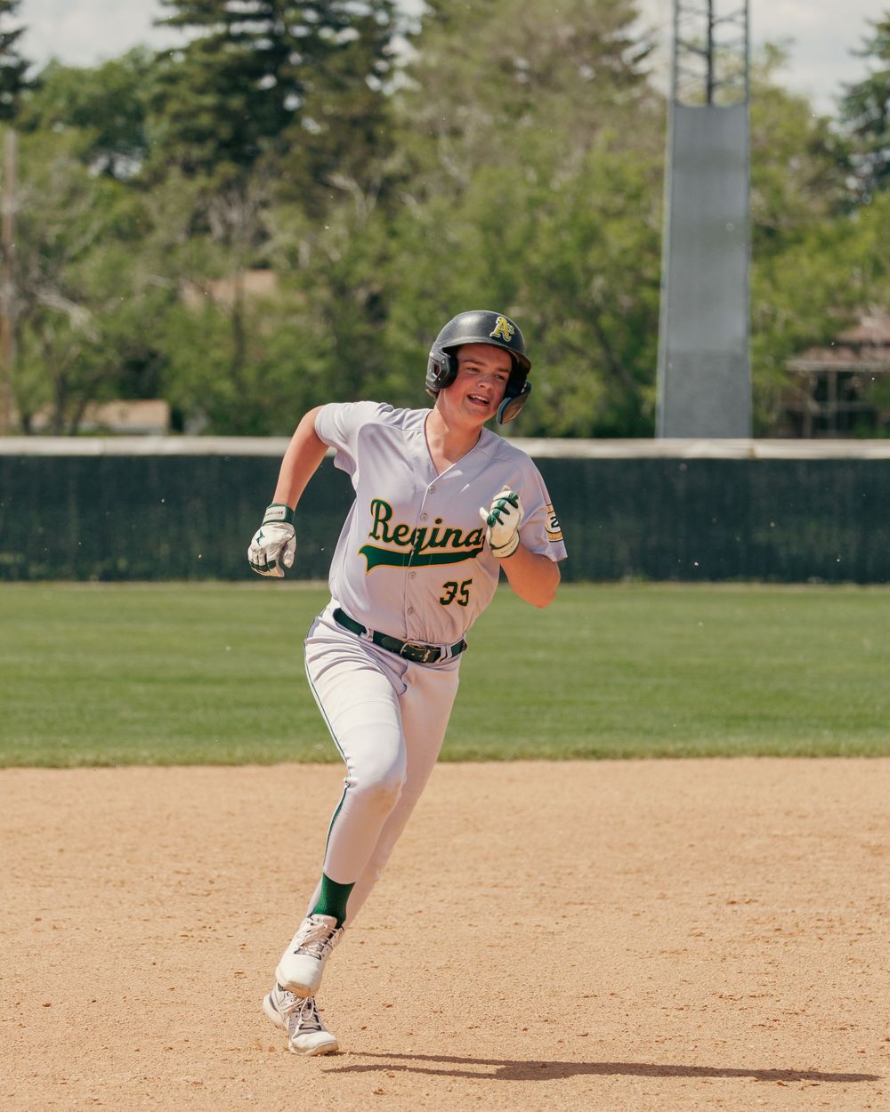 Regina baseball player number 35 in white uniform sprints around second base with a smile.