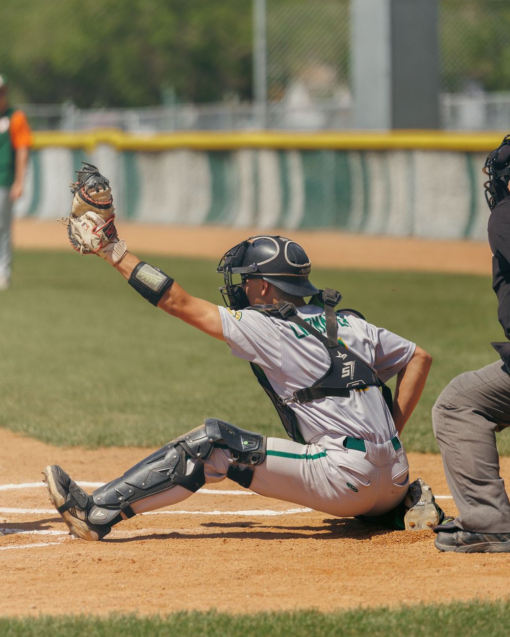 Regina baseball catcher in full gear stretches to tag out runner at home plate during game.