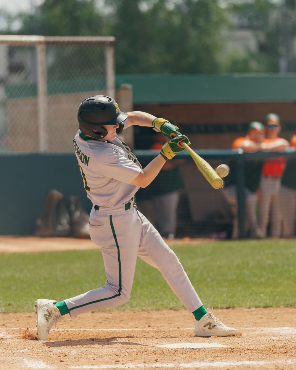 A youth baseball player in a green uniform swings a bat during a game.