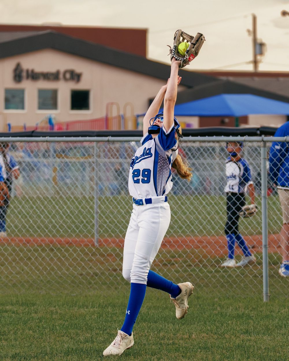 A Royals outfielder wearing number 29 leaps to catch a softball near the outfield fence.