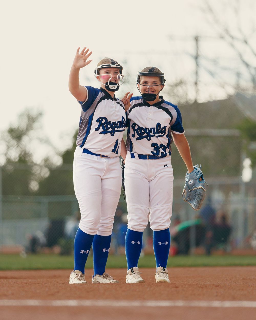 Two Royals softball players celebrate together on the field during a game.