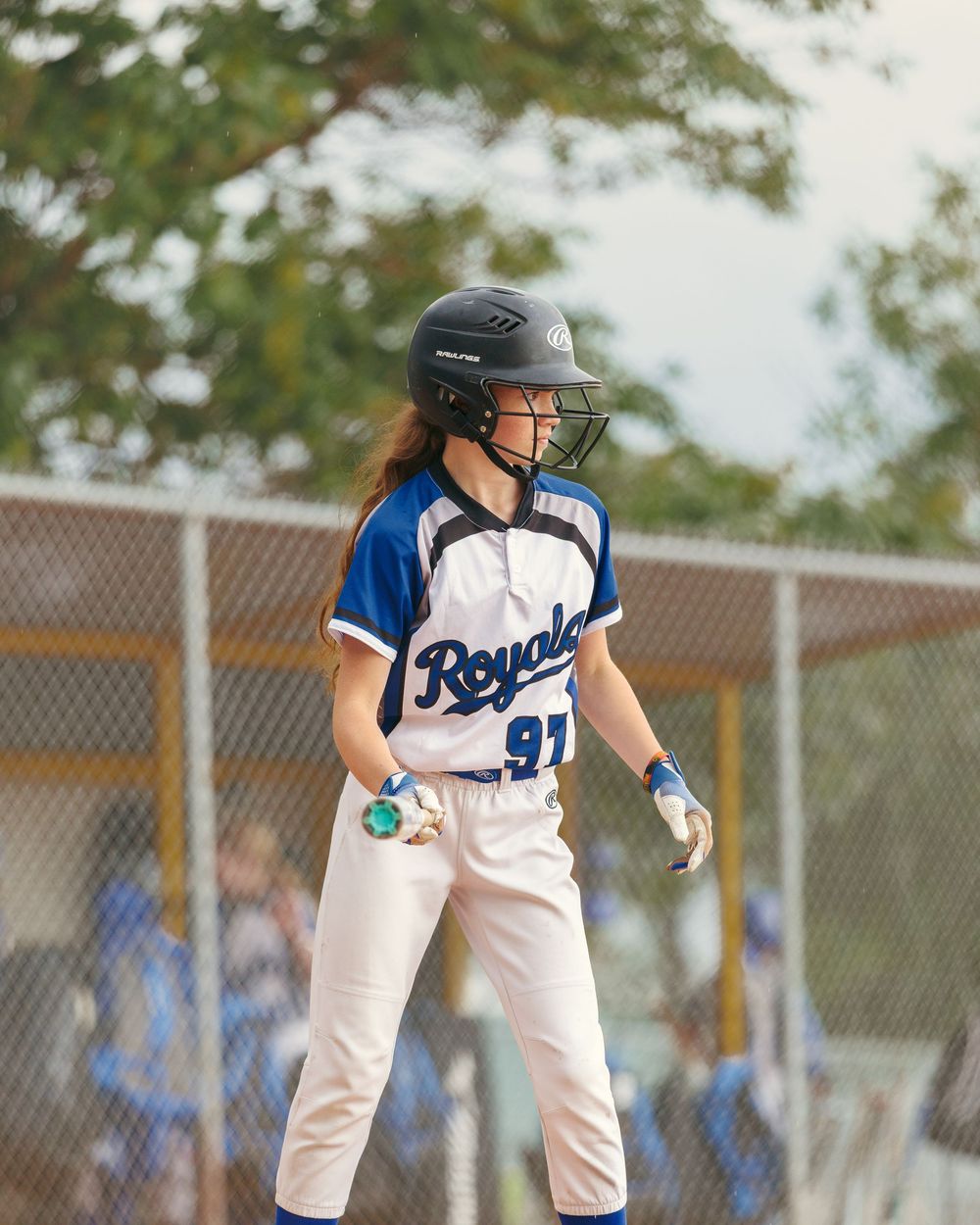 A young softball player in a Royals uniform and helmet stands ready at bat during a game.