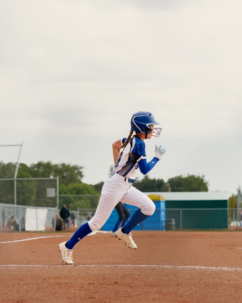 A female softball player in a blue Royals uniform sprints along the baseline during a game.