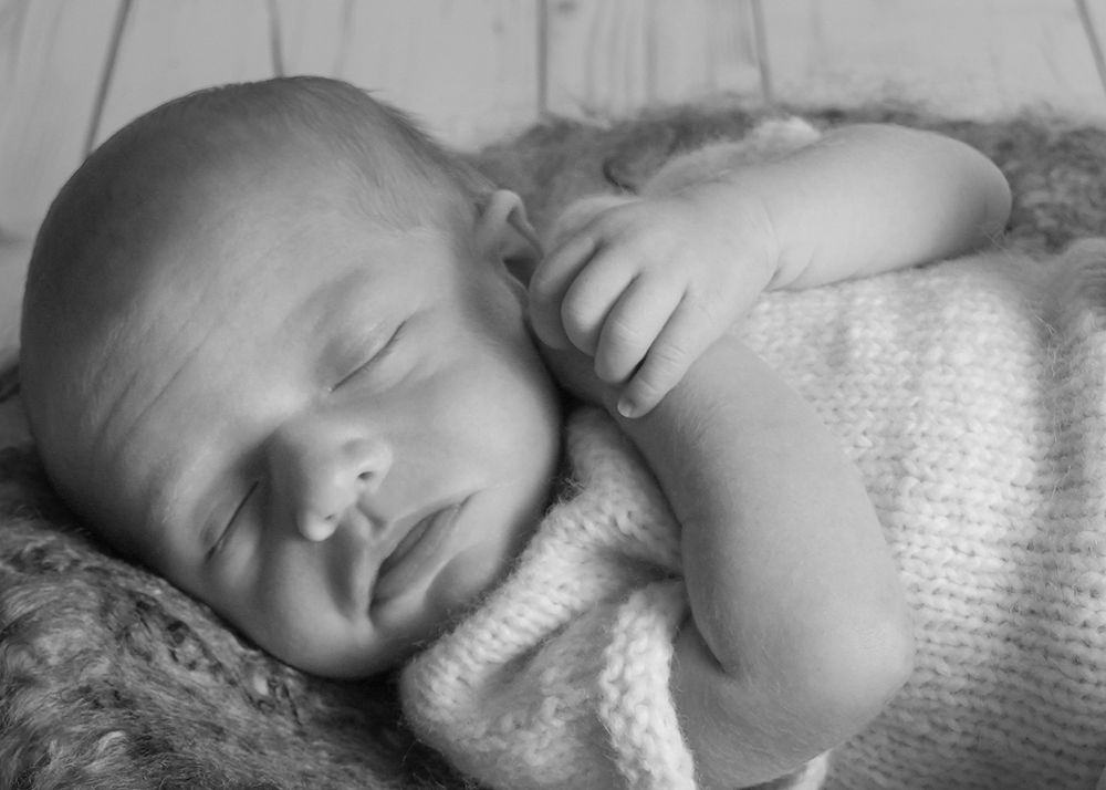 Black and white newborn baby sleeping peacefully wrapped in a knit blanket on a soft furry surface.