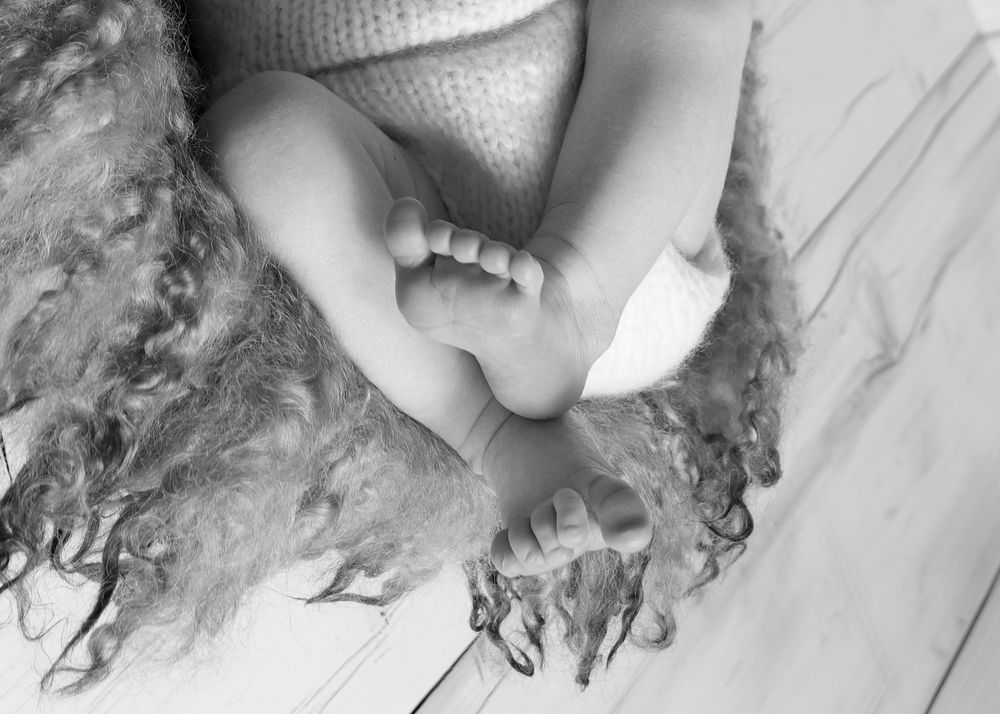 Black and white close-up photo of a newborn baby's tiny feet and toes resting on a soft fluffy blanket.