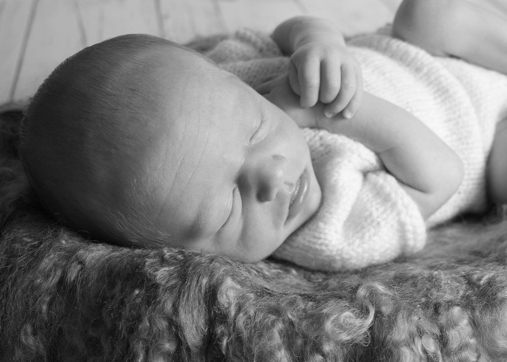 Black and white photo of a peaceful sleeping newborn baby lying on a soft fluffy blanket.