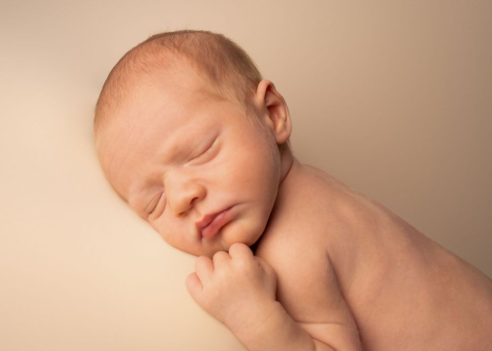 Peaceful newborn baby sleeping on a soft beige background in a professional newborn photography portrait.
