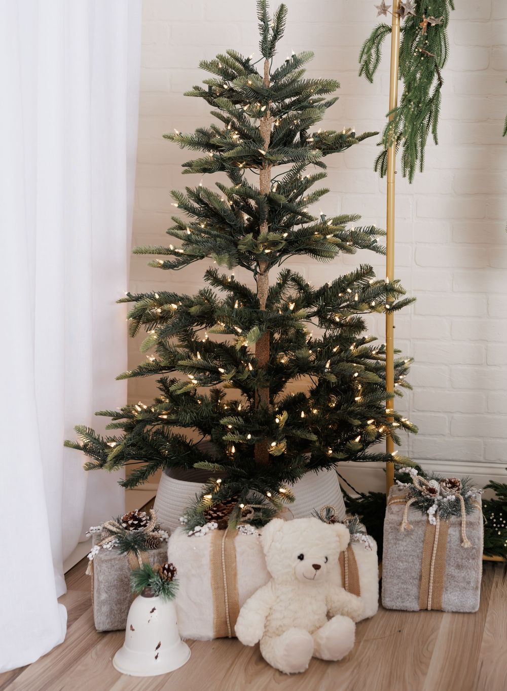 A decorated Christmas tree with warm lights, wrapped gifts, and a white teddy bear on a wooden floor.