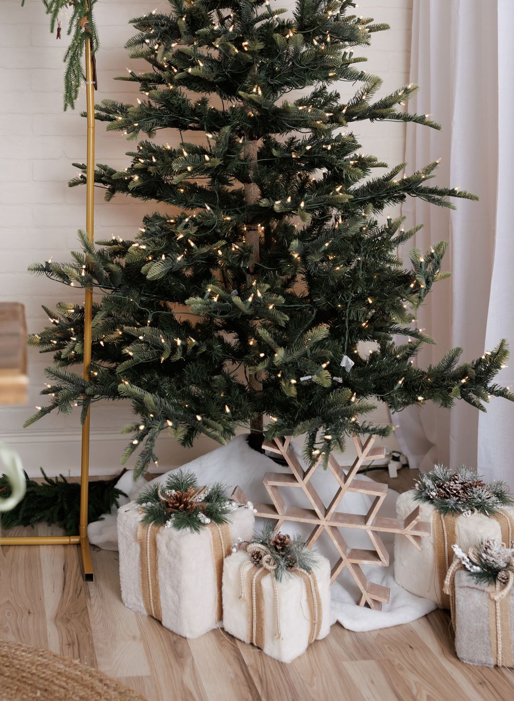 A decorated Christmas tree with warm fairy lights, white wrapped gifts, and a wooden snowflake ornament on a white tree skirt.
