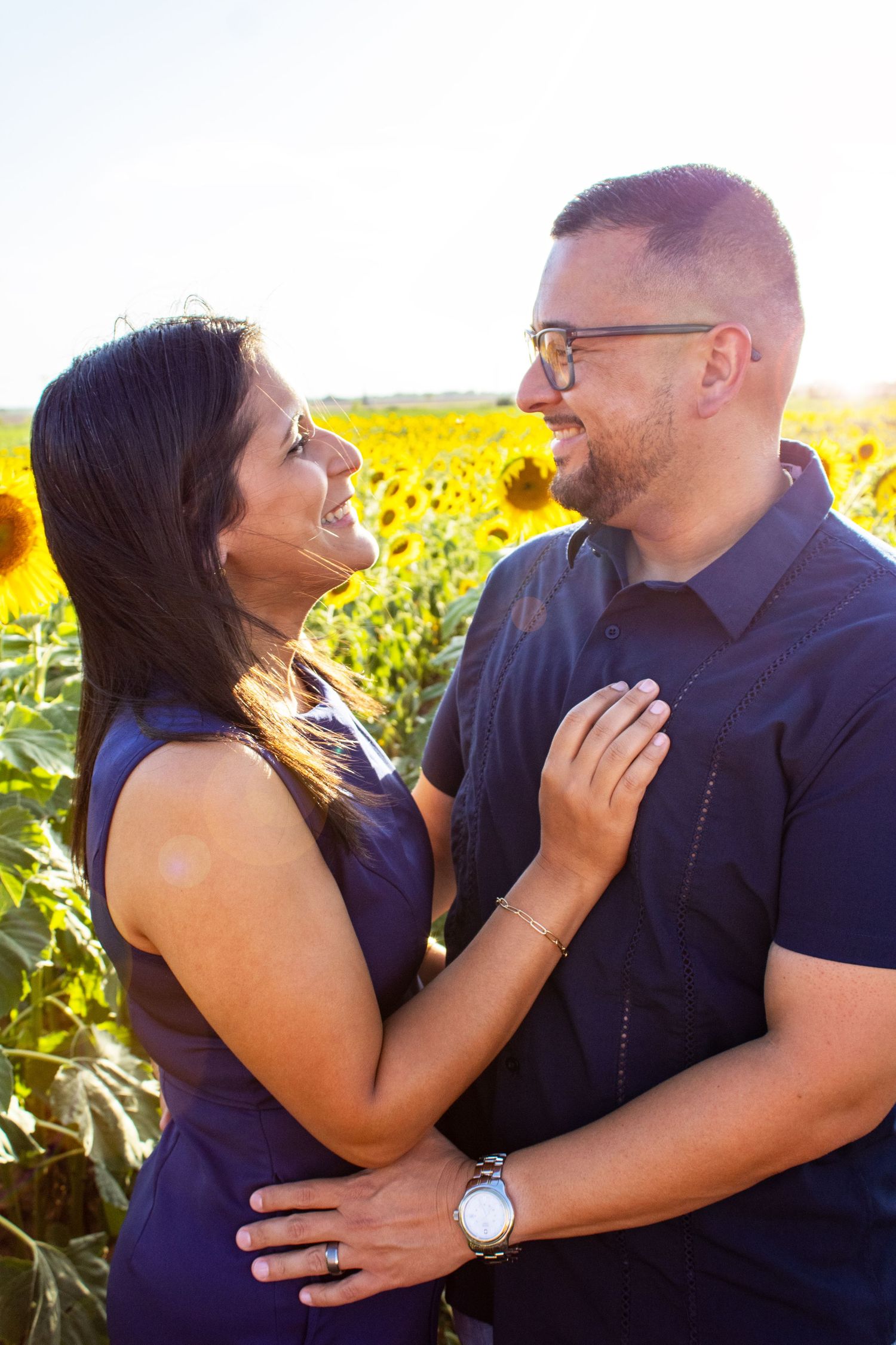 Happy couple embracing and smiling in sunny sunflower field.