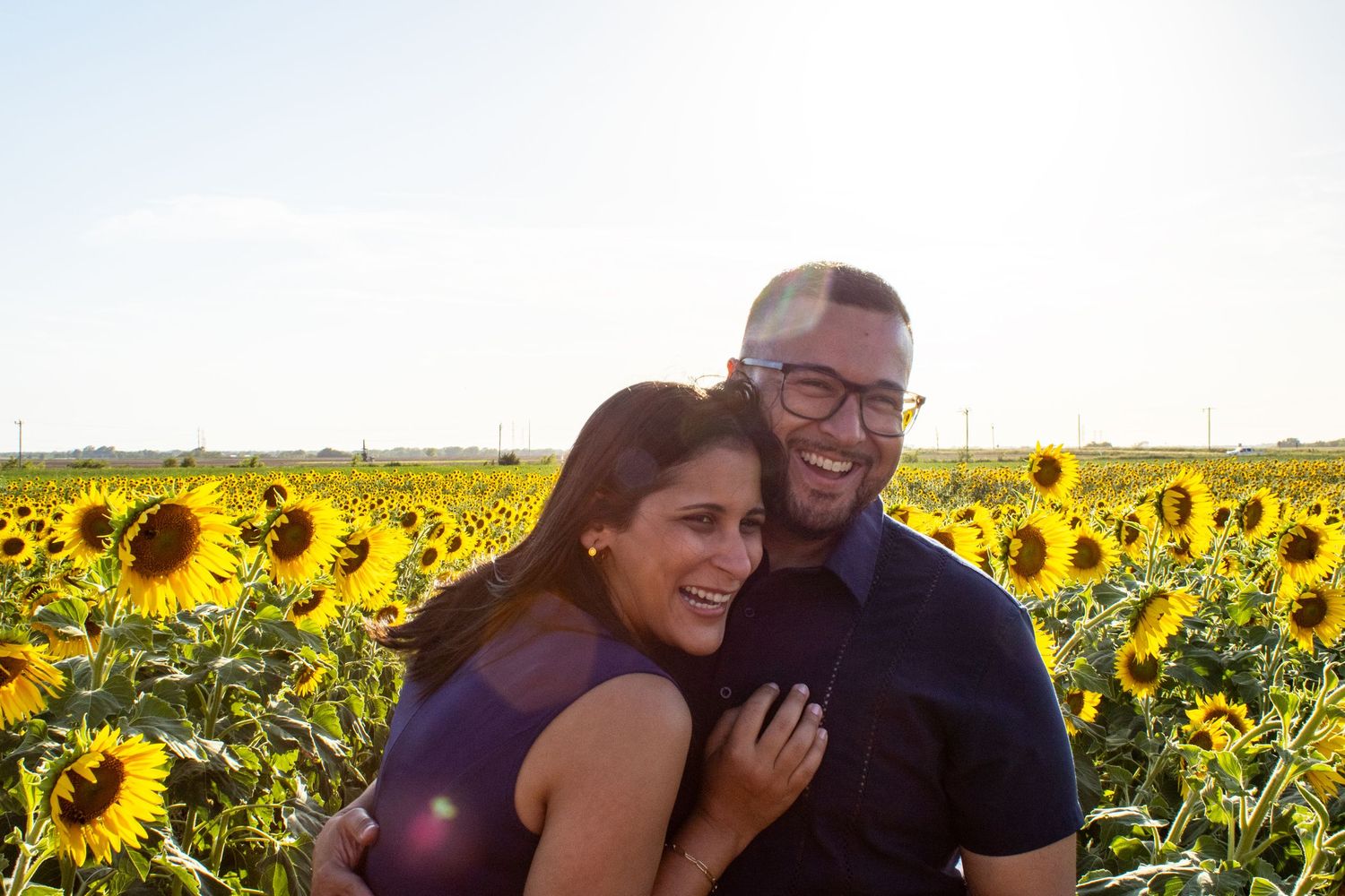 Couple laughing together in a vibrant sunflower field during golden hour sunset.