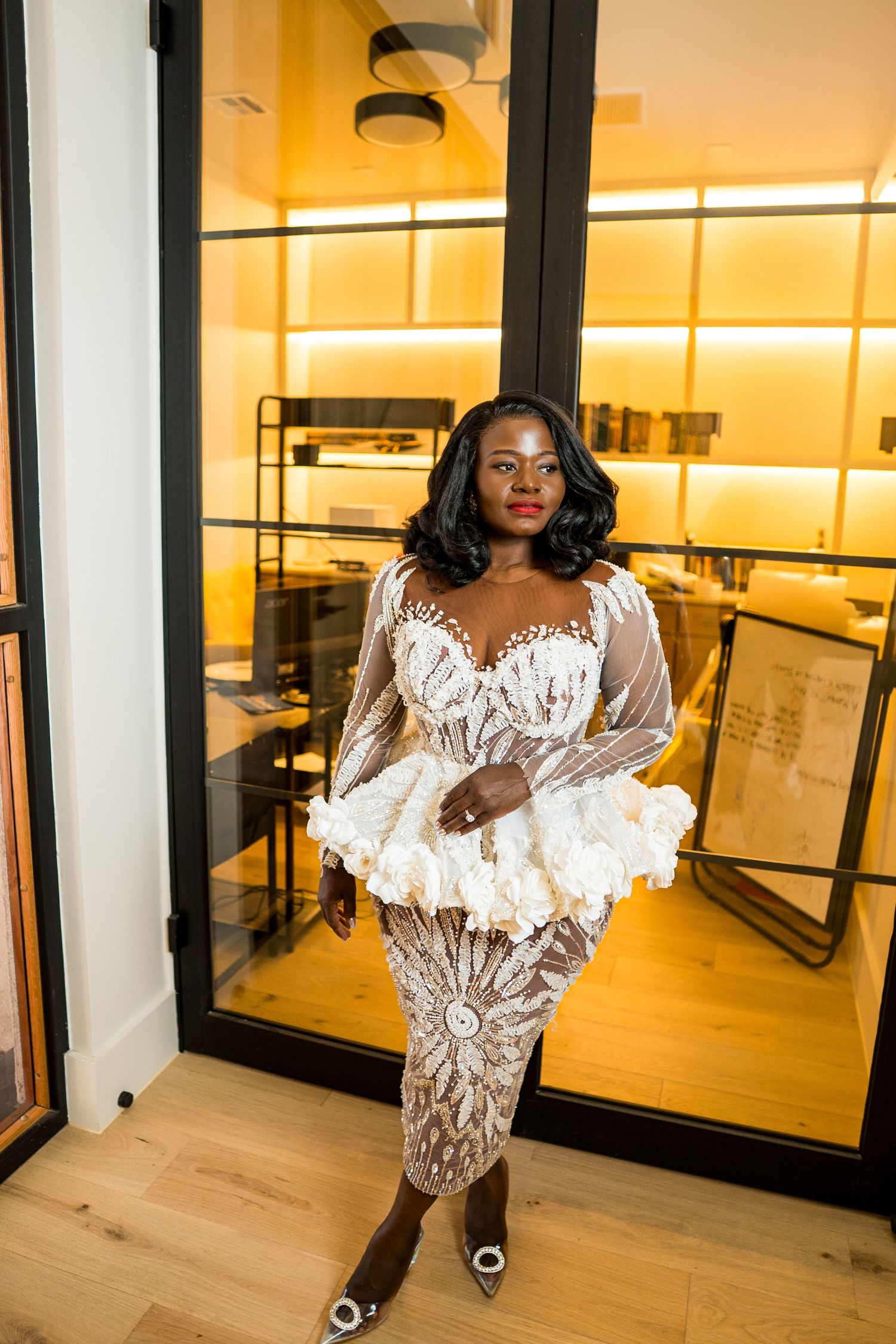 Woman in elegant white lace midi dress with ruffle peplum posing in modern interior setting.