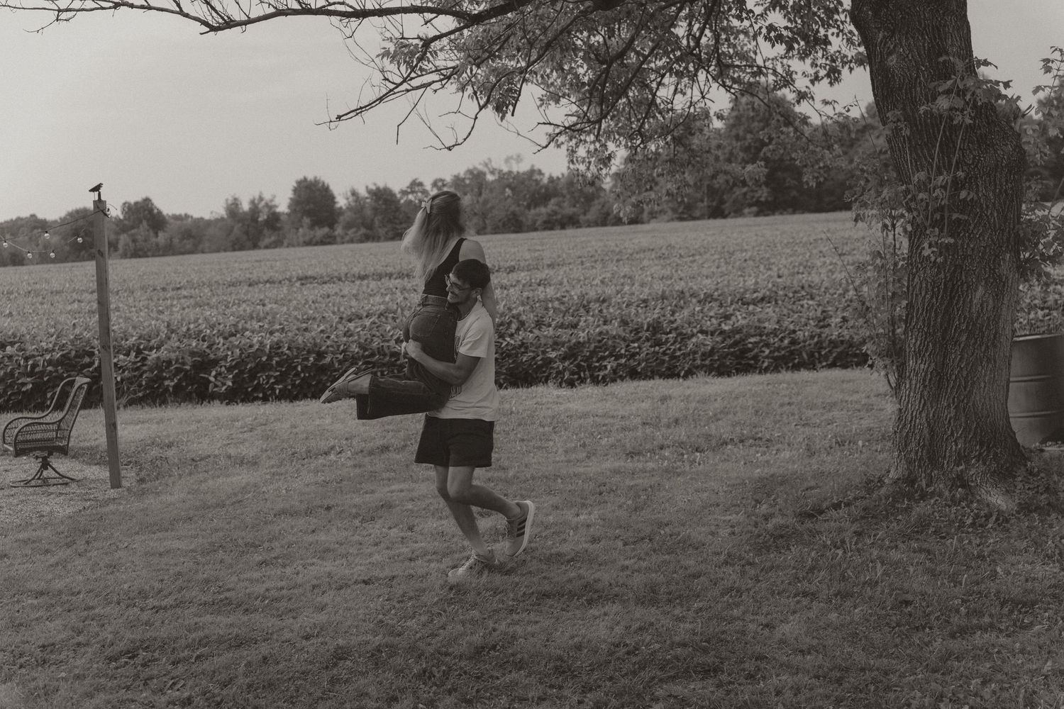Black and white photo of two children playing near a large tree in a rural field on a sunny day.