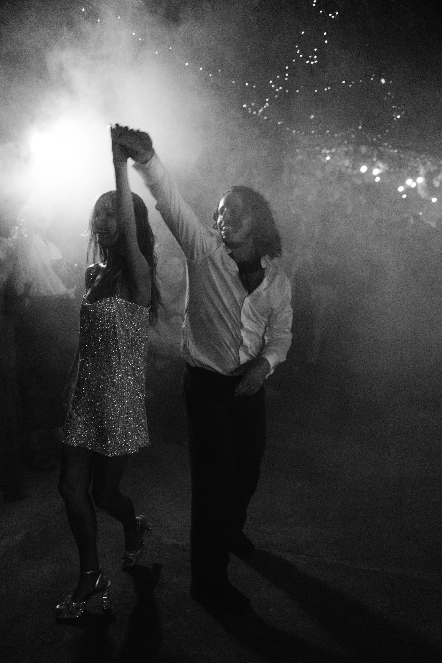 Couple dancing elegantly in black and white photo with dramatic smoke and bokeh lights in background.