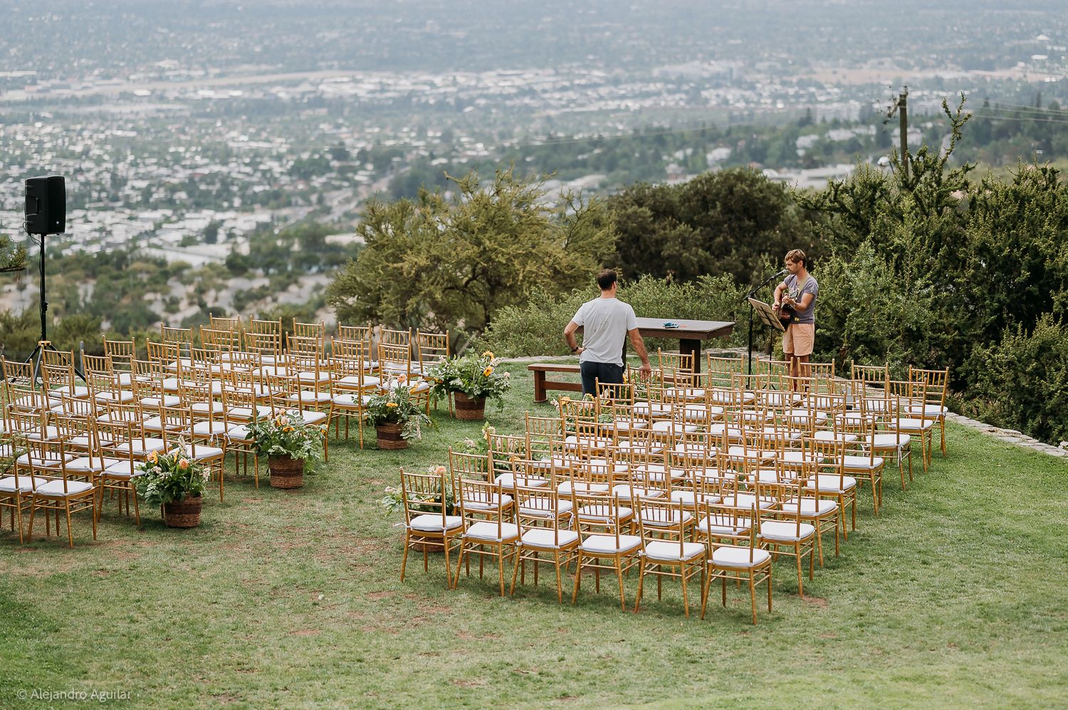 Outdoor wedding ceremony setup with gold chairs on a hillside overlooking a scenic valley landscape.
