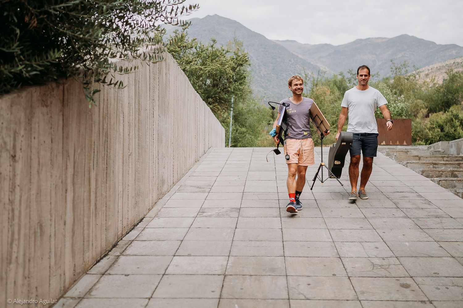 Two men walking on a tiled pathway with golf bags, mountains and trees in the background.