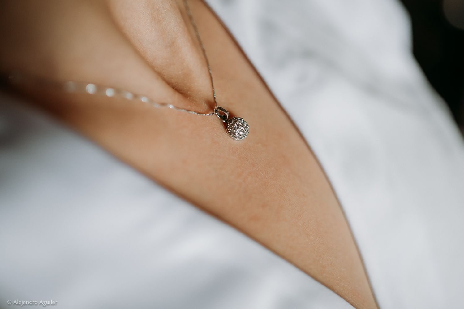 Close-up of a delicate rose gold necklace with a diamond pendant resting on a bride's décolletage.