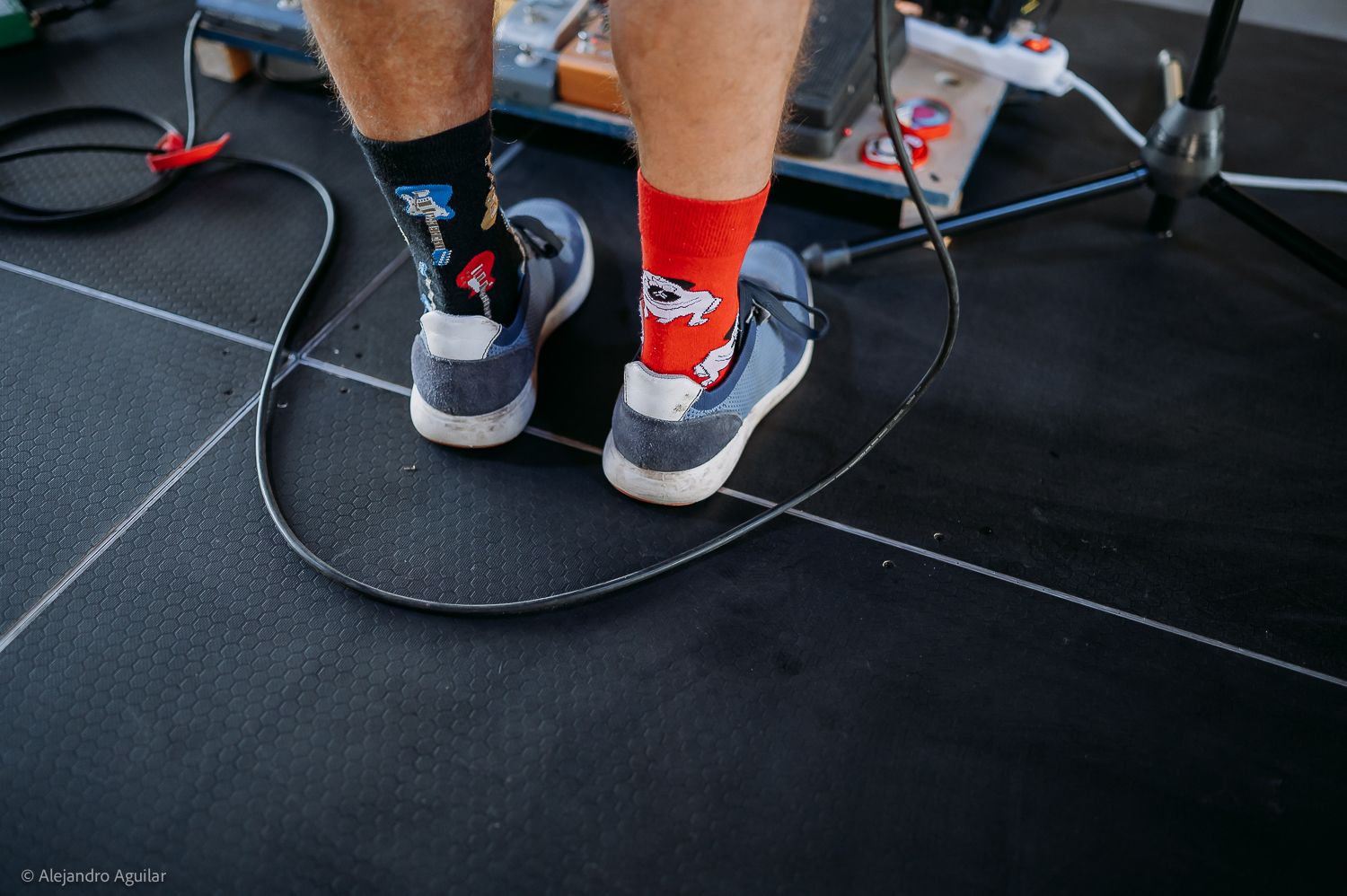 Close-up of person wearing red socks and sneakers standing on black gym mat with cables around feet.
