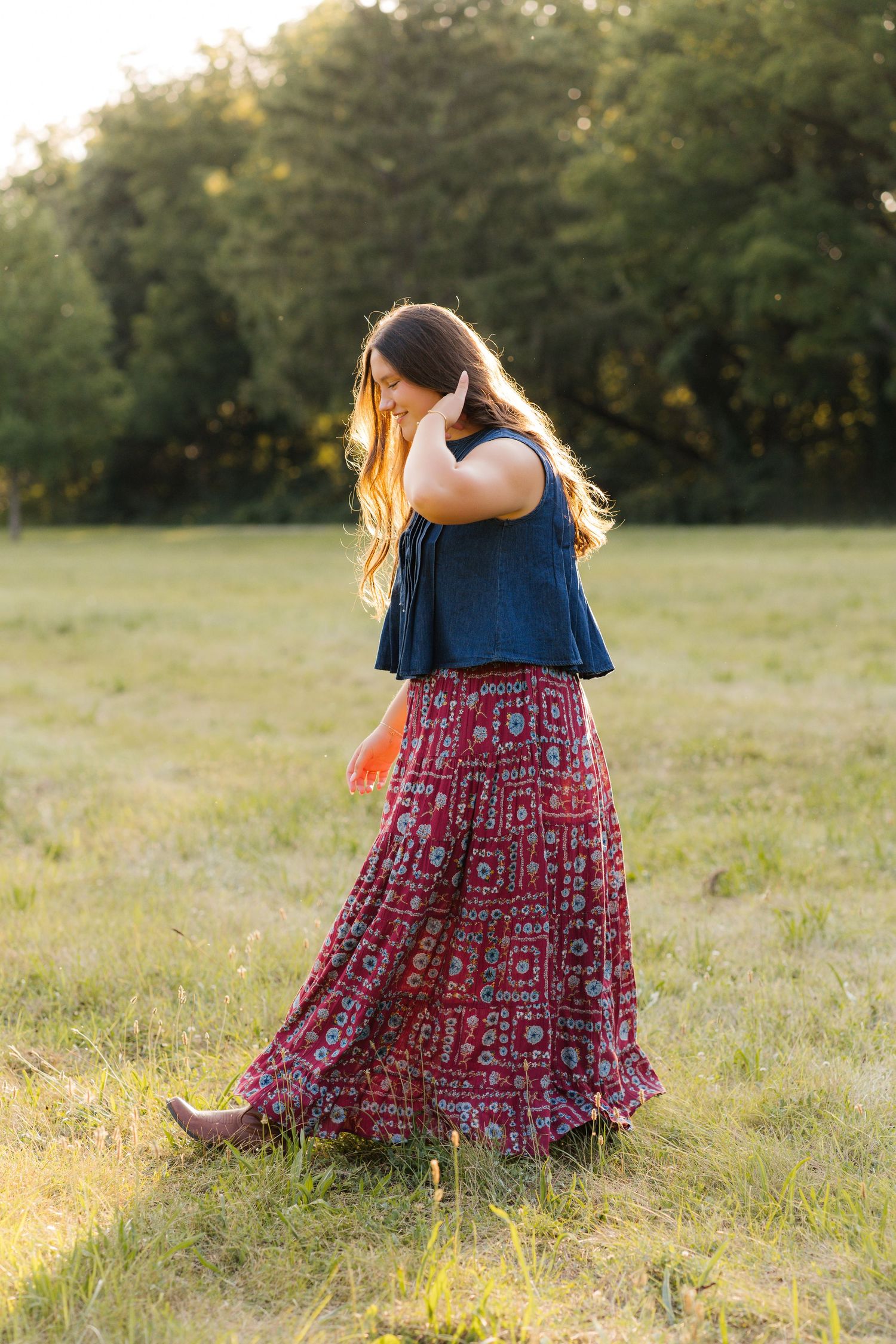 Woman in navy crop top and red boho maxi skirt walking in sunlit green field.