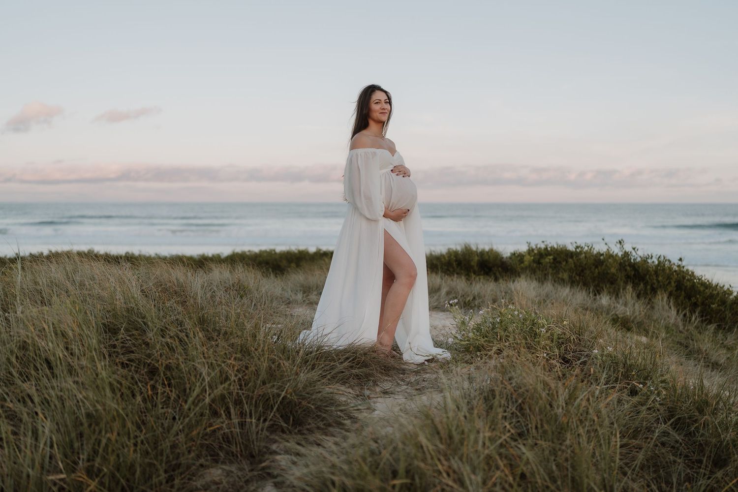 Pregnant woman posing dressed in white flowing dress at the beach in Wollongong NSW