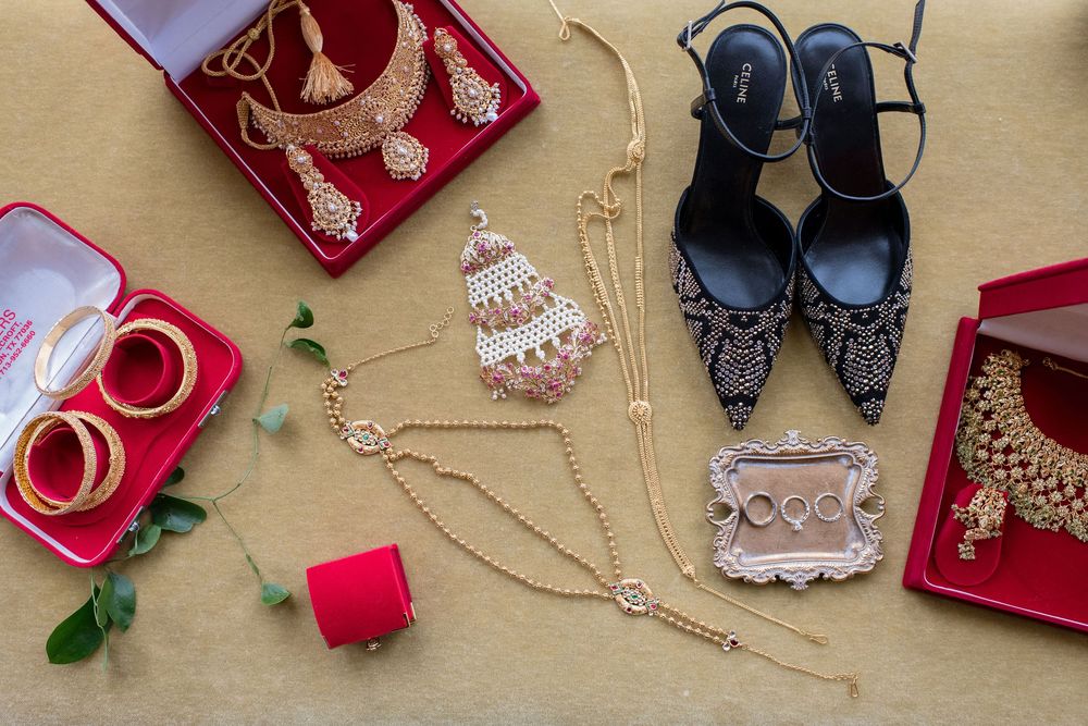 Elegant bridal accessories flatlay featuring gold jewelry, bangles, embellished heels, and necklaces on a beige background.