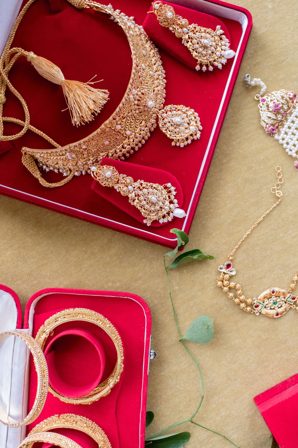 Elegant Indian bridal jewelry set with gold necklace, earrings, and bangles displayed in red velvet boxes.