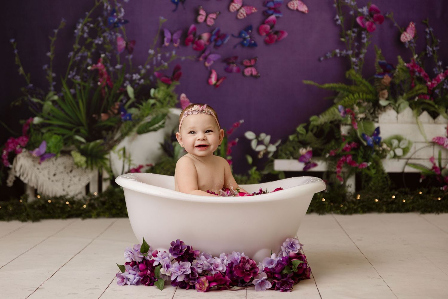 Smiling baby in a white tub surrounded by purple flowers and butterflies