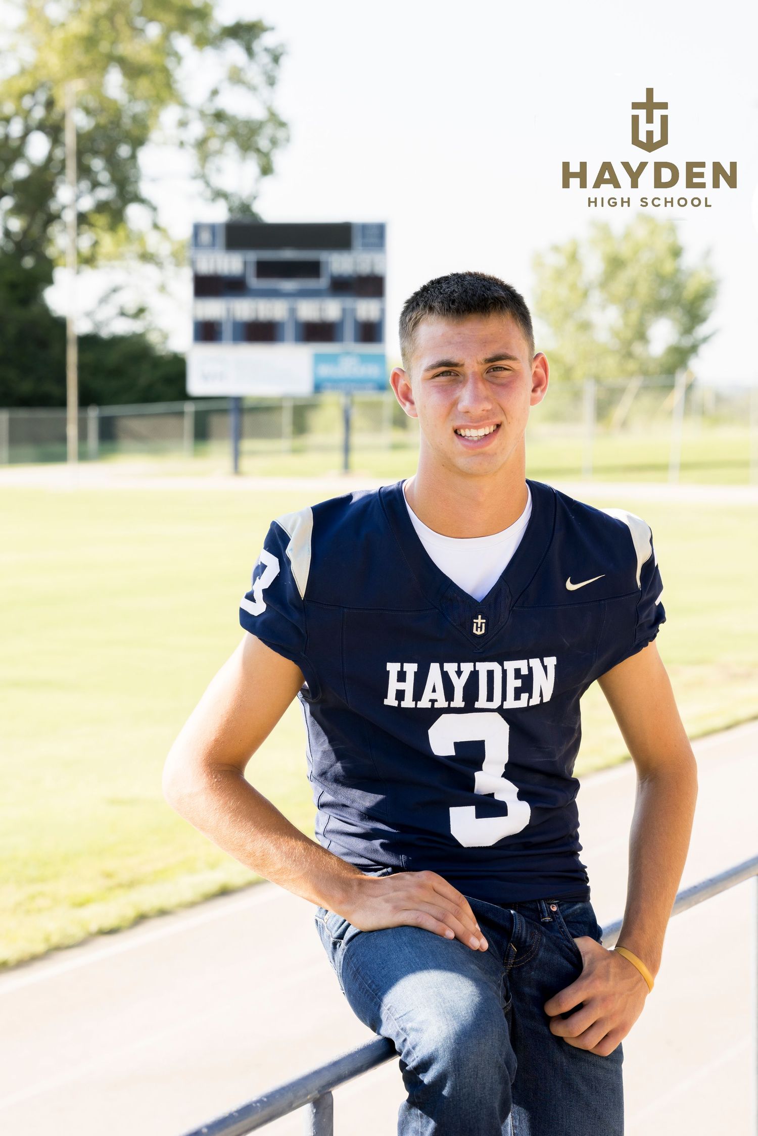 Hayden High School football player wearing navy jersey number 3, posing on field with scoreboard in background.