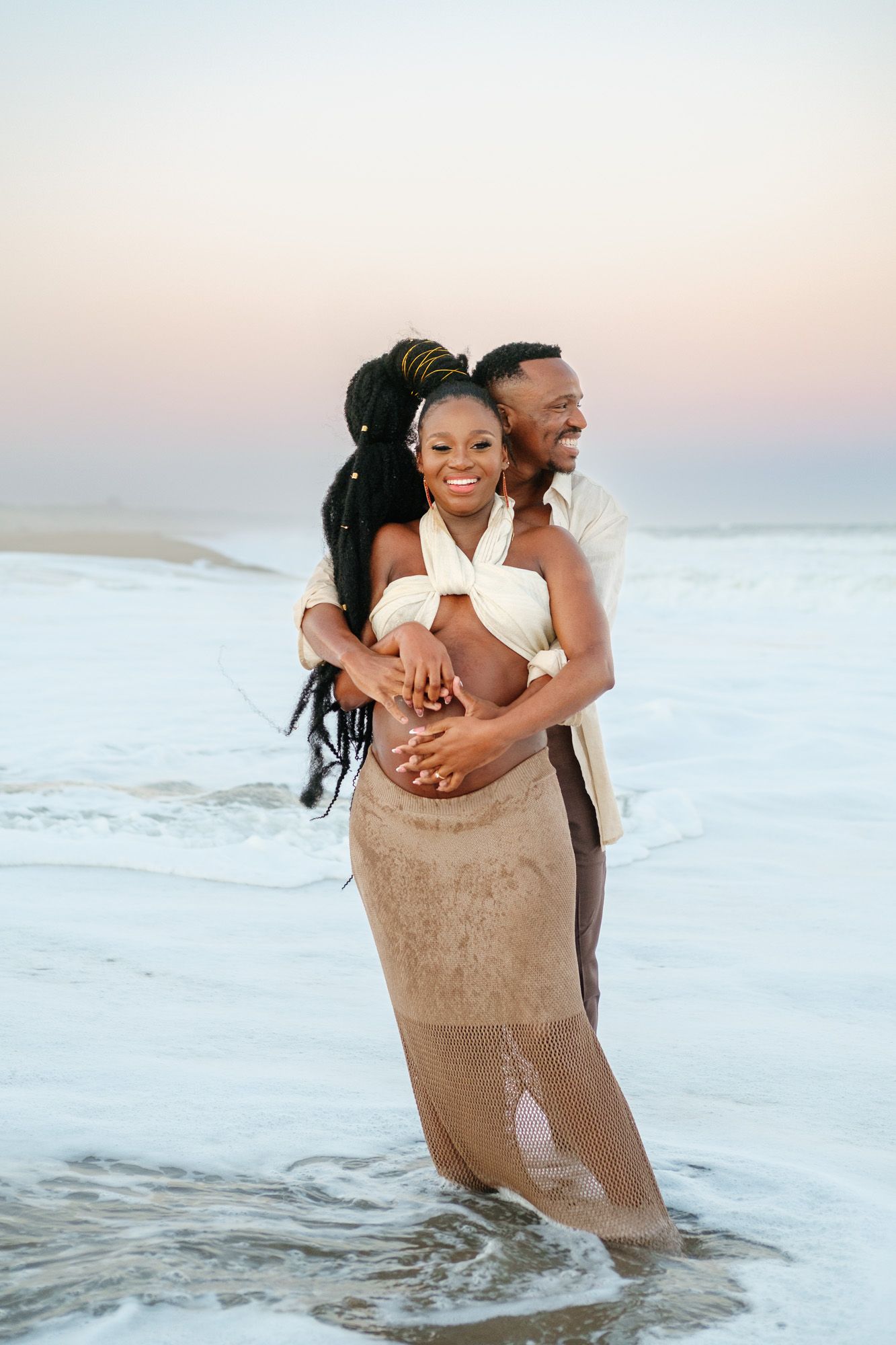 Pregnant woman and her partner laughing together with the sea in the background