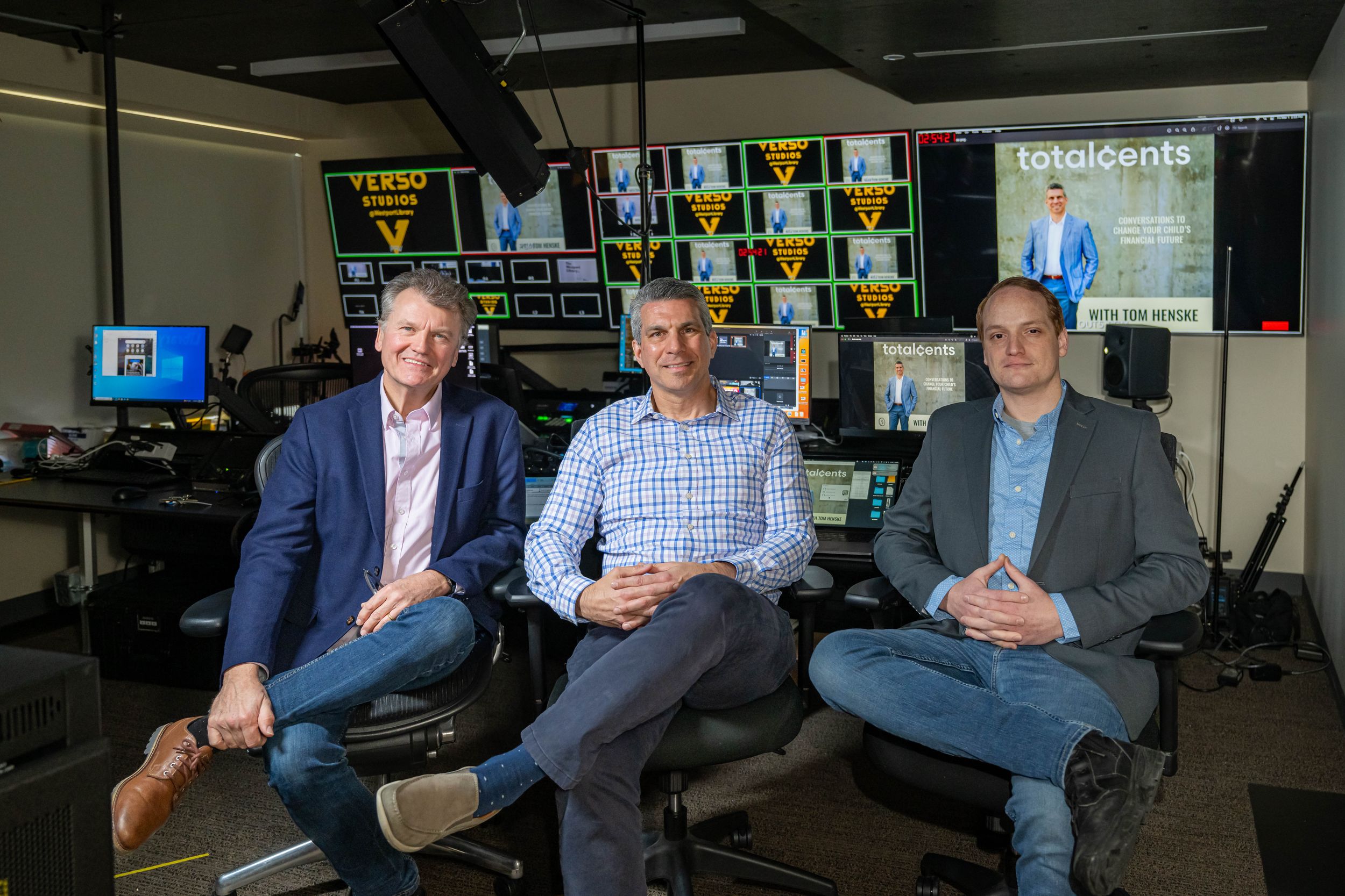 Three business professionals pose in a modern media control room with multiple screens displaying content.