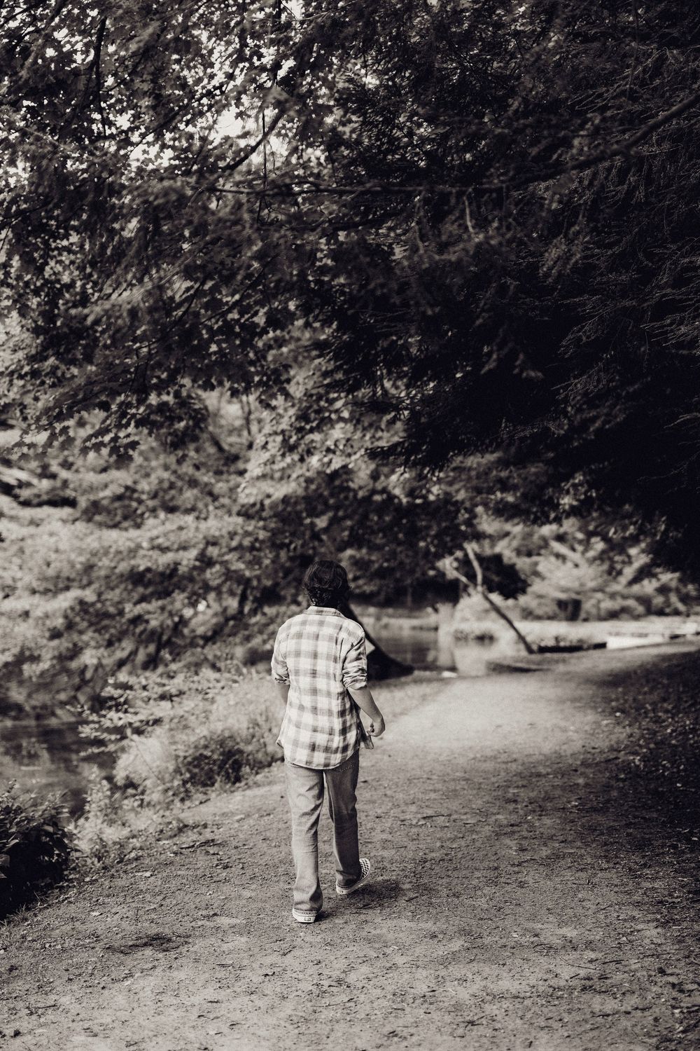 Black and white photo of a person walking along a forest path near a tranquil stream.