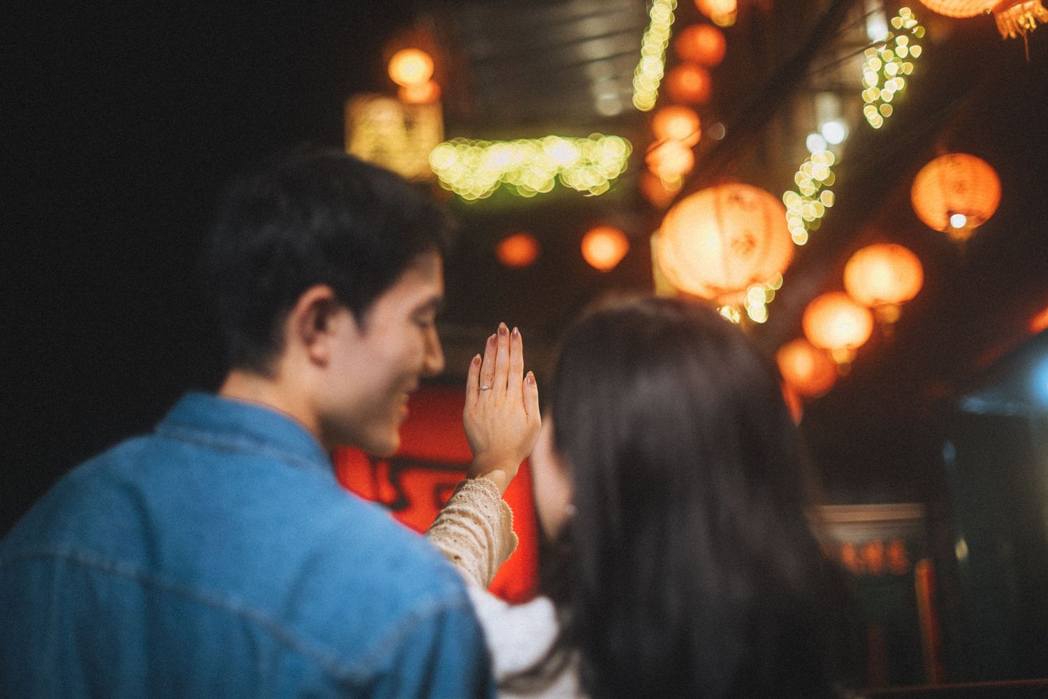Couple praying with hands together at a Chinese lantern festival at night.