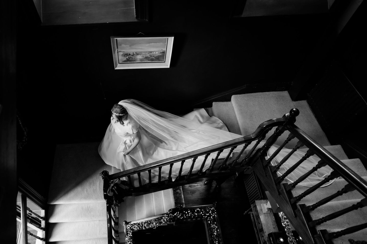 Black and white photo of a bride in a flowing gown and veil descending an elegant wooden staircase at Boyne Hill House, Co. Meath