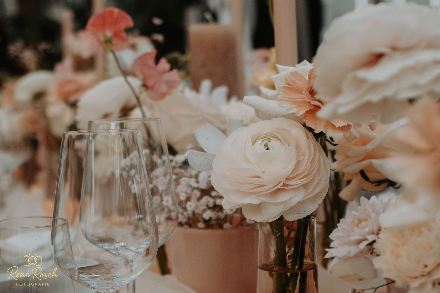 Elegant wedding table centerpiece with blush pink ranunculus and soft floral arrangements in glass vases.
