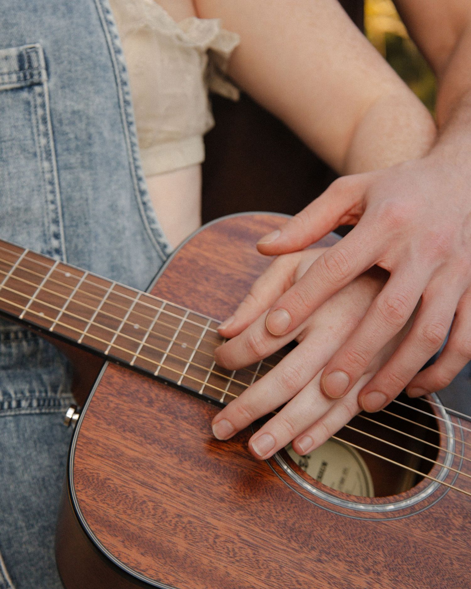 Two hands resting together on the strings of a wooden ukulele.