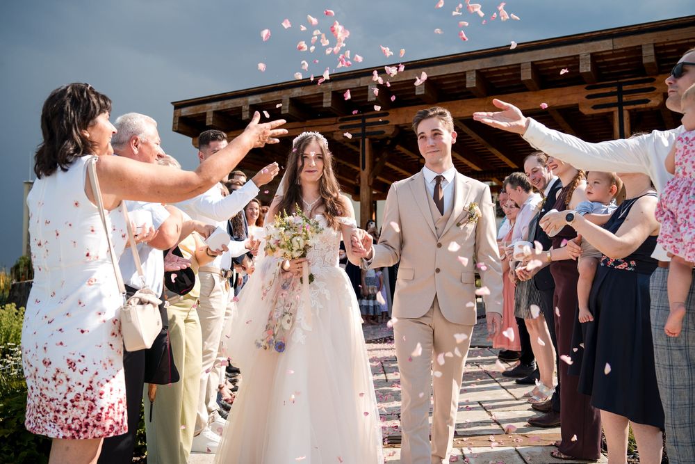 Newlyweds walk through confetti shower as guests celebrate their wedding ceremony outdoors.