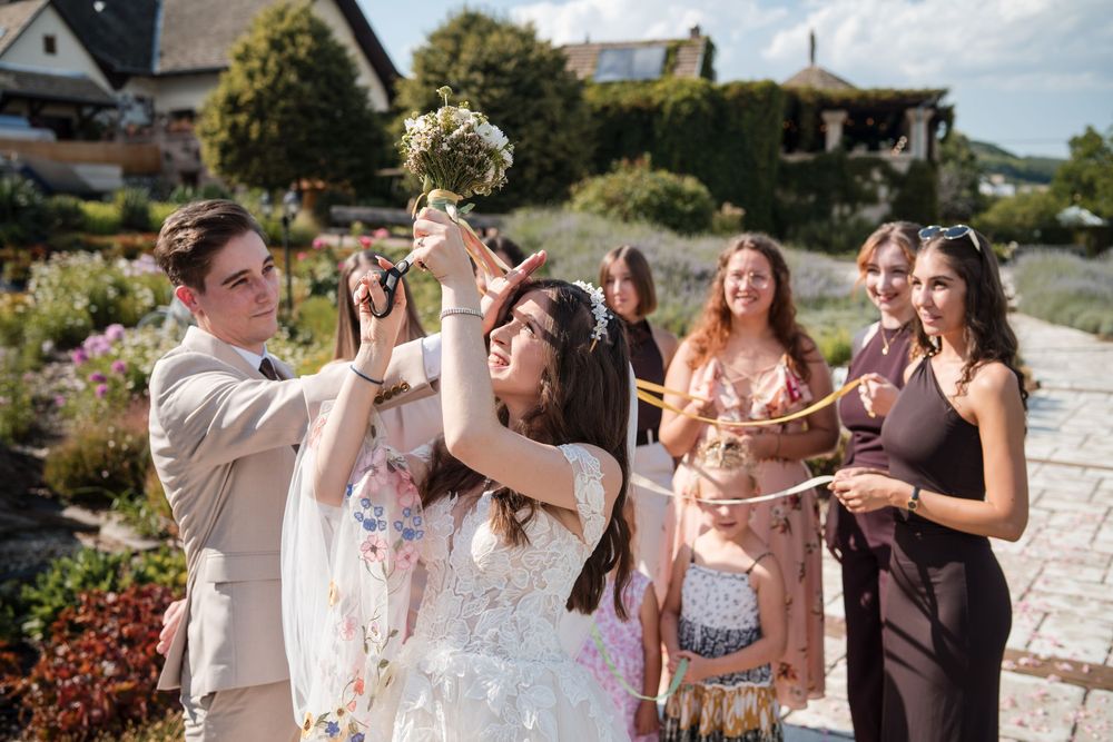 Bride tossing bouquet to excited guests outdoors at a sunny garden wedding celebration.