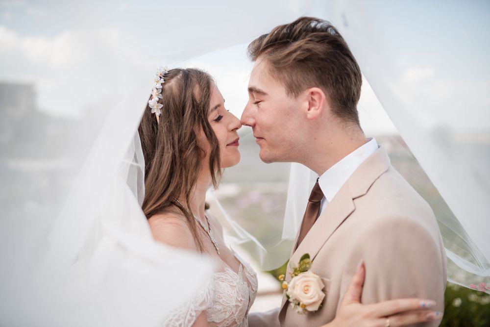 Bride and groom share a romantic moment under a flowing veil on their wedding day.