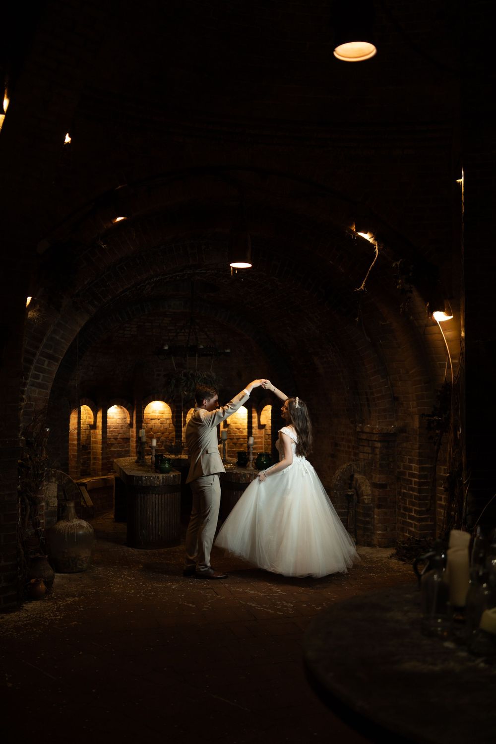 Bride and groom dancing in a romantic candlelit brick wine cellar tunnel during their wedding celebration.