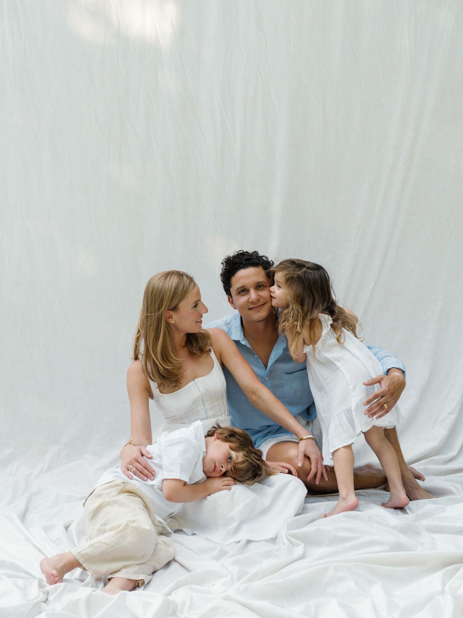 Family cuddling on a white bed with their young child during a Dallas lifestyle session