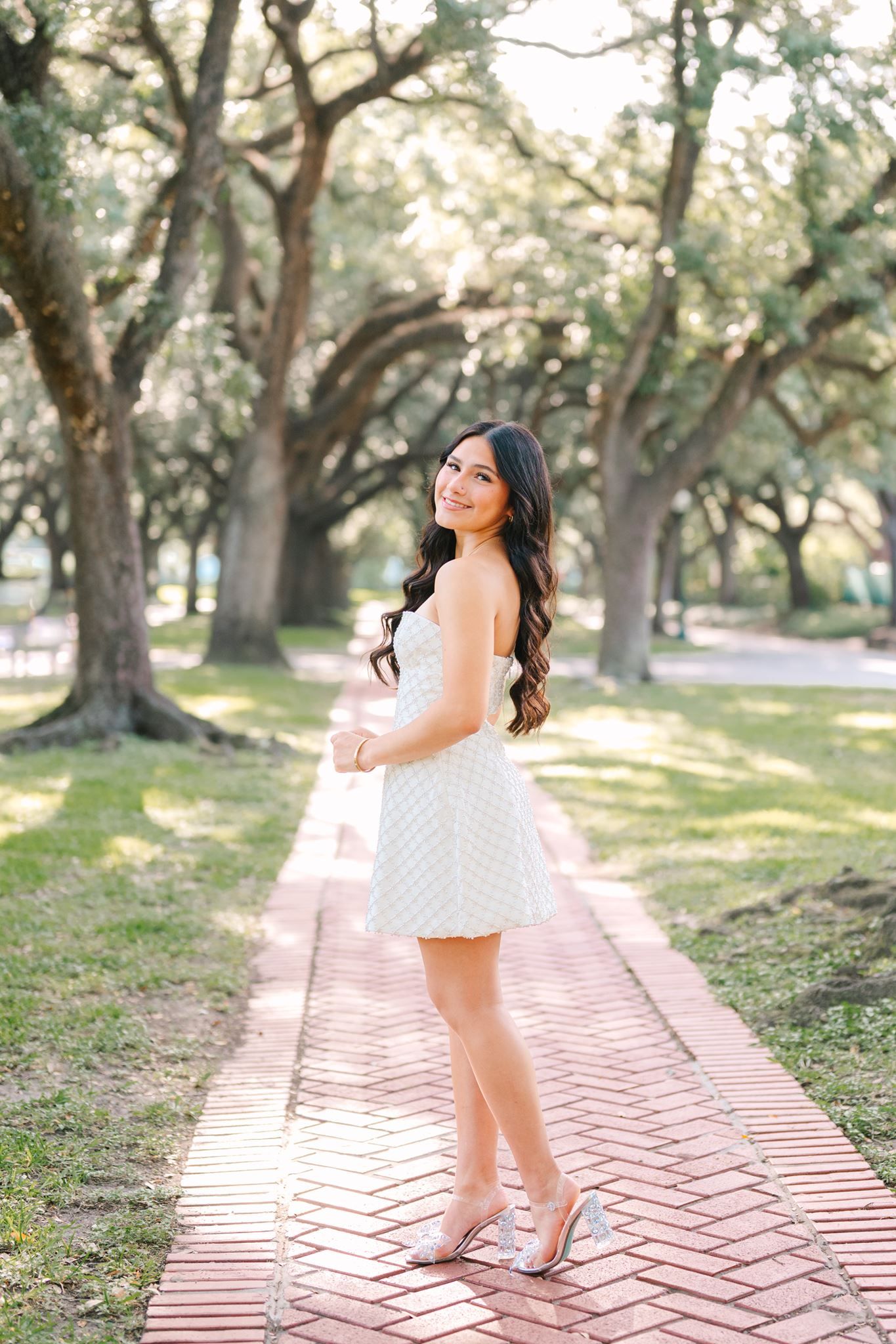 College Park High School senior girl, wearing short white dress, standing under oak tree canopy in Houston Texas.