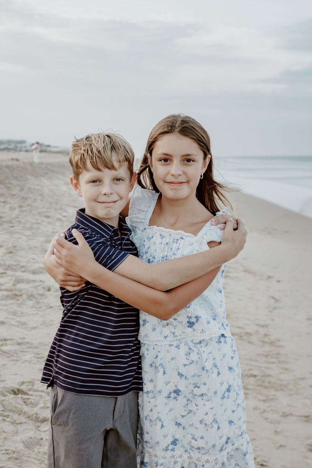 Young boy and girl share a warm hug together on sandy beach during family portrait session. Sandbridge.