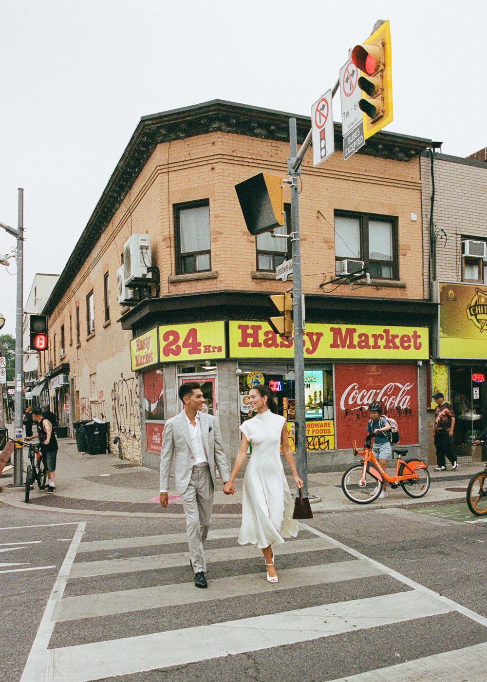Couple holding hands crossing a street in front of a 24hrs Happy Market with Coca-Cola sign in urban city.