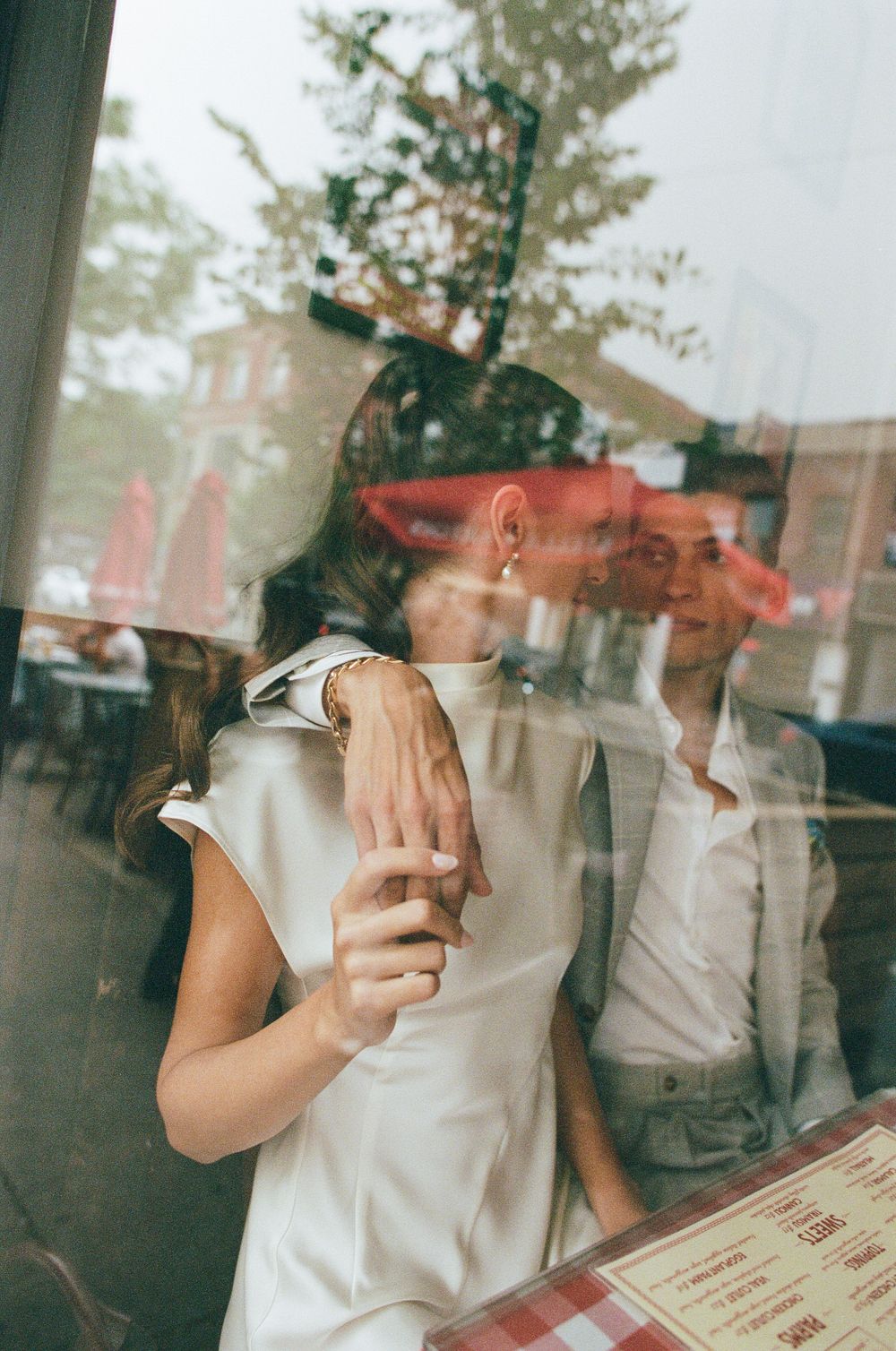 Couple sharing a romantic moment inside a restaurant, viewed through a reflective window.