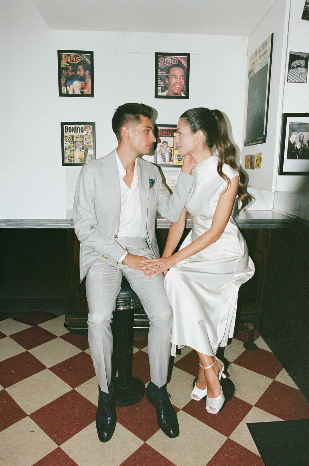Couple in elegant white and grey outfits sitting together in a vintage diner with boxing posters on the wall.