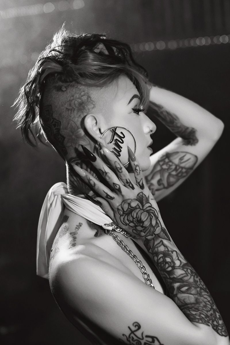 Black and white portrait showcasing artistic sleeve tattoos and an edgy hairstyle in dramatic lighting.